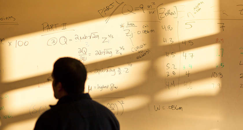 A student studies an equation on a whiteboard. 